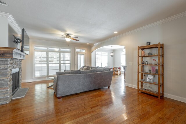 living room with ceiling fan with notable chandelier, crown molding, a fireplace, and hardwood / wood-style floors