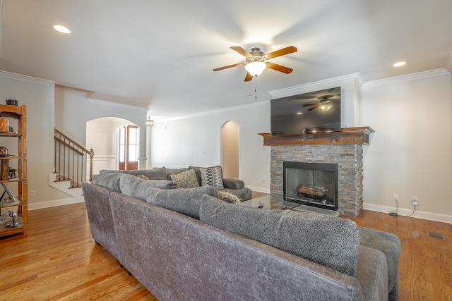 living room featuring light hardwood / wood-style flooring, ceiling fan, crown molding, and a stone fireplace