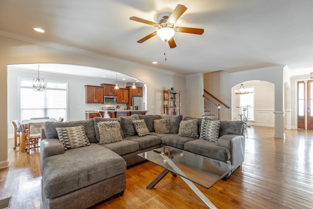 living room featuring ornamental molding, ceiling fan with notable chandelier, and wood-type flooring