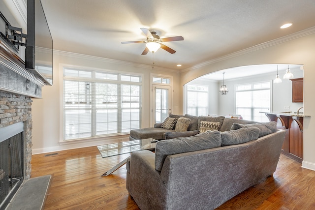 living room with a fireplace, crown molding, ceiling fan with notable chandelier, and wood-type flooring