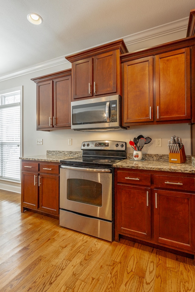 kitchen with light stone counters, stainless steel appliances, light hardwood / wood-style floors, and ornamental molding