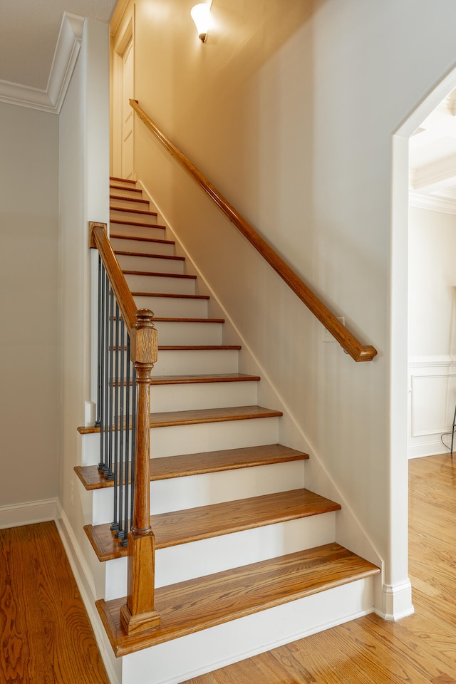 staircase with ornamental molding and hardwood / wood-style floors