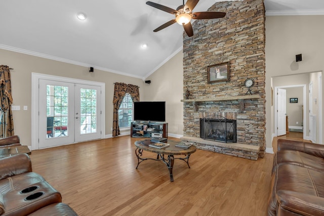 living room featuring light wood-type flooring, ceiling fan, ornamental molding, and a stone fireplace