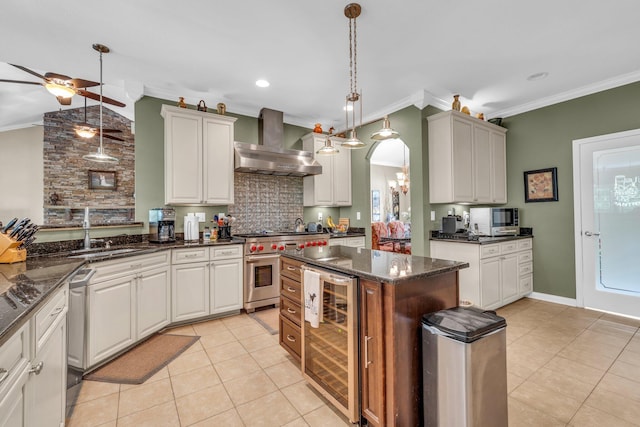 kitchen with ceiling fan with notable chandelier, stainless steel appliances, wall chimney range hood, dark stone counters, and wine cooler