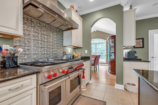 kitchen featuring range with two ovens, premium range hood, light hardwood / wood-style floors, crown molding, and dark stone countertops