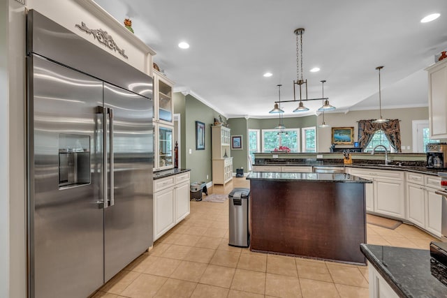 kitchen featuring dark stone counters, decorative light fixtures, built in fridge, a kitchen island, and white cabinets