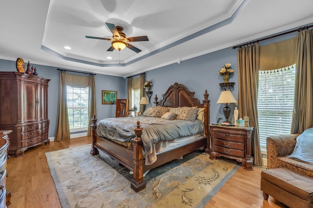 bedroom with light wood-type flooring, a tray ceiling, and ceiling fan