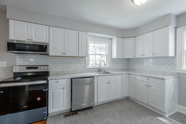 kitchen with sink, appliances with stainless steel finishes, white cabinets, and light tile patterned flooring