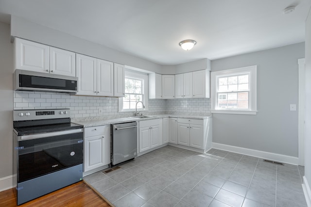 kitchen with appliances with stainless steel finishes, sink, white cabinetry, and a healthy amount of sunlight