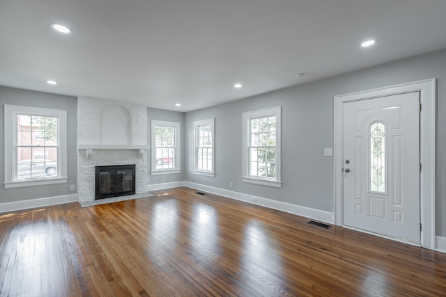 foyer entrance featuring dark wood-type flooring, plenty of natural light, and a stone fireplace