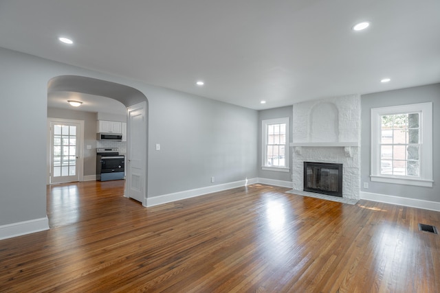 unfurnished living room with dark wood-type flooring and a stone fireplace