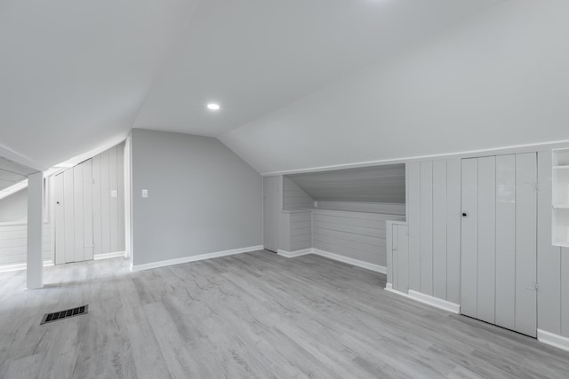 additional living space with light wood-type flooring, lofted ceiling, and wooden walls