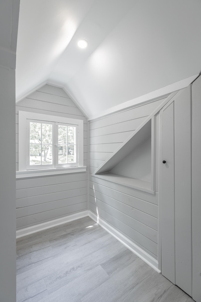 additional living space with lofted ceiling, wood walls, and light hardwood / wood-style flooring