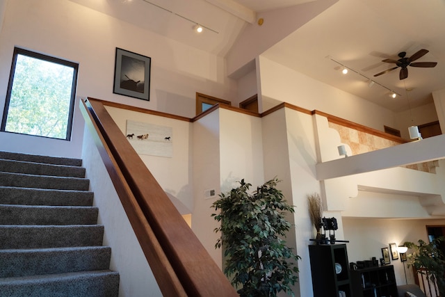 stairway with ceiling fan, track lighting, and high vaulted ceiling