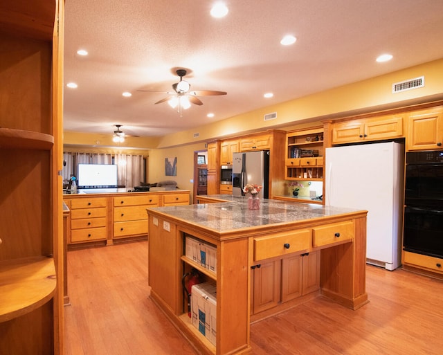 kitchen featuring appliances with stainless steel finishes, ceiling fan, a textured ceiling, a kitchen island, and light wood-type flooring