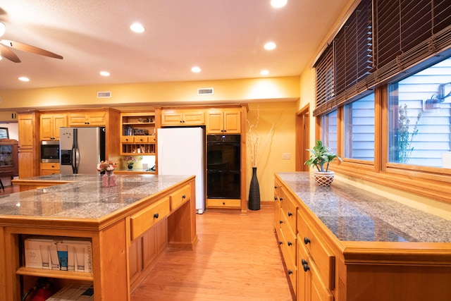 kitchen with white refrigerator, a large island, stainless steel refrigerator with ice dispenser, double oven, and light hardwood / wood-style flooring