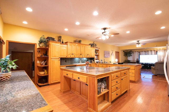 kitchen featuring a center island with sink, tasteful backsplash, light brown cabinetry, ceiling fan, and light hardwood / wood-style flooring