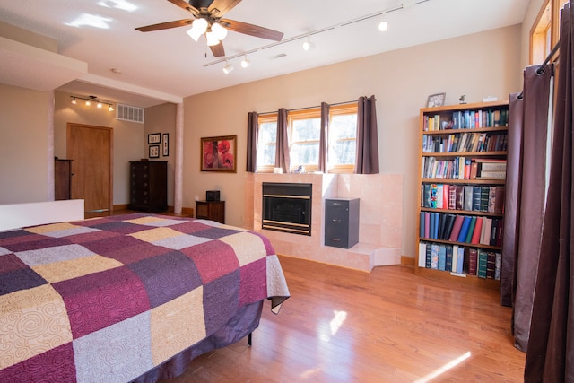 bedroom with a tiled fireplace, track lighting, light hardwood / wood-style floors, and ceiling fan