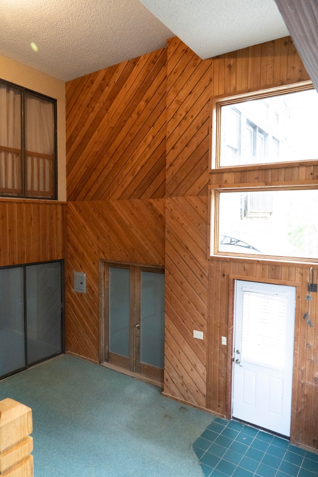 interior space featuring wooden walls, a textured ceiling, dark carpet, and plenty of natural light