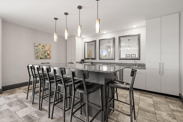 kitchen featuring dark stone countertops, a breakfast bar area, decorative light fixtures, and white cabinets