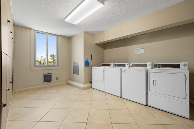 washroom with light tile patterned flooring, heating unit, independent washer and dryer, and a textured ceiling