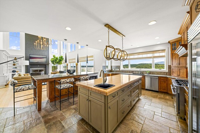 kitchen with stainless steel appliances, a center island with sink, a notable chandelier, and a brick fireplace