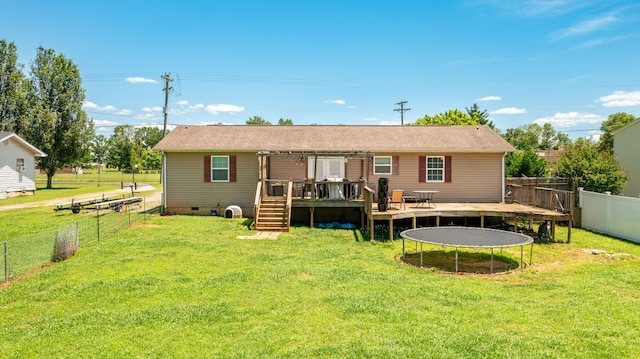 back of house with a yard, a wooden deck, and a trampoline