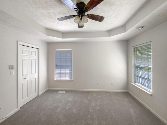 carpeted spare room with a textured ceiling, ceiling fan, and a tray ceiling