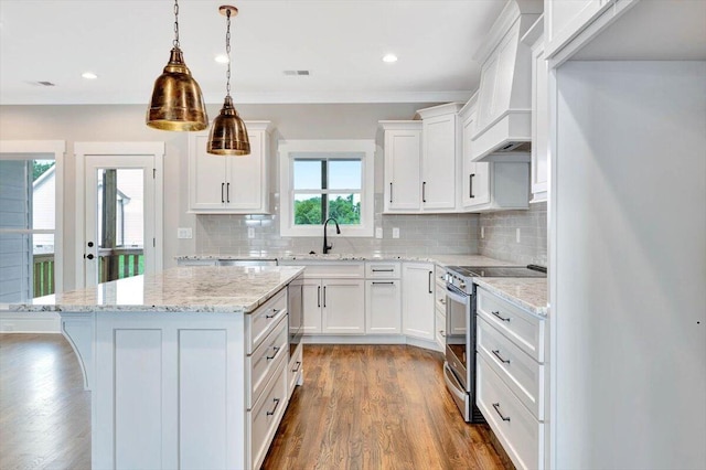 kitchen with stainless steel electric range, white cabinets, light stone countertops, premium range hood, and wood-type flooring