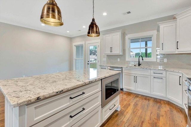 kitchen featuring light wood finished floors, a sink, decorative backsplash, white cabinets, and stainless steel microwave
