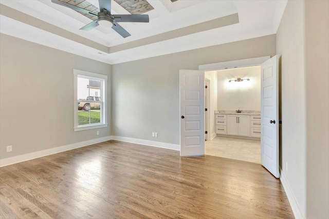 unfurnished bedroom featuring ceiling fan, a raised ceiling, light hardwood / wood-style floors, and ensuite bathroom