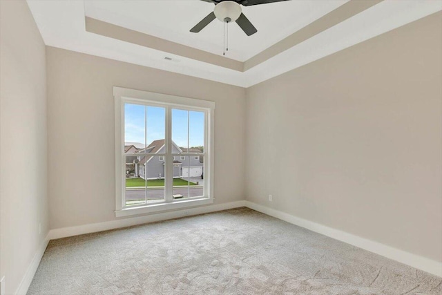 carpeted spare room with visible vents, ceiling fan, a raised ceiling, and baseboards
