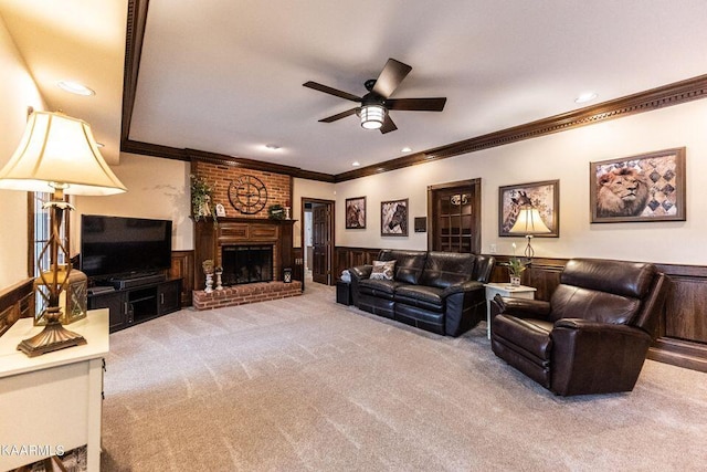 carpeted living area with a ceiling fan, a wainscoted wall, recessed lighting, a fireplace, and crown molding