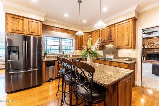 kitchen with brown cabinetry, light stone countertops, stainless steel fridge, and ornamental molding