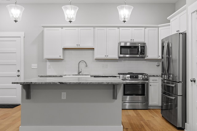 kitchen featuring tasteful backsplash, a sink, light wood-style floors, light stone countertops, and appliances with stainless steel finishes
