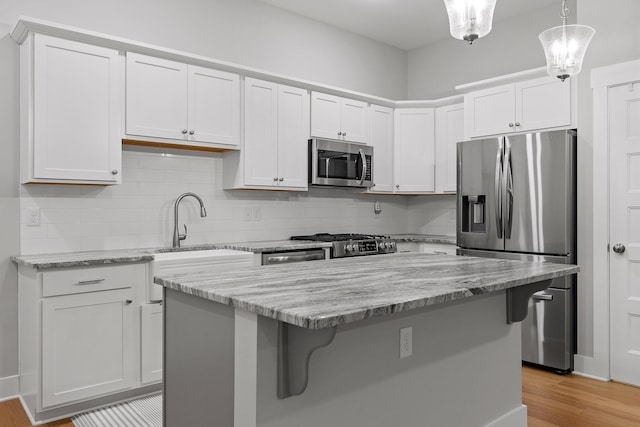 kitchen with a kitchen bar, tasteful backsplash, light stone counters, white cabinets, and appliances with stainless steel finishes