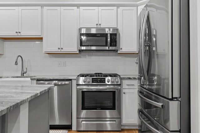 kitchen with backsplash, light stone countertops, stainless steel appliances, white cabinetry, and sink