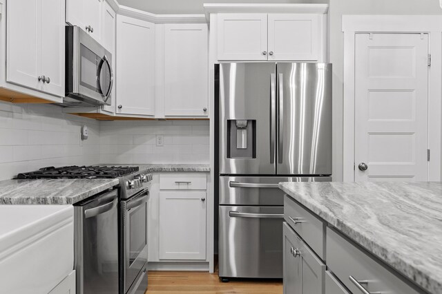 kitchen featuring light wood-type flooring, tasteful backsplash, light stone countertops, appliances with stainless steel finishes, and white cabinets