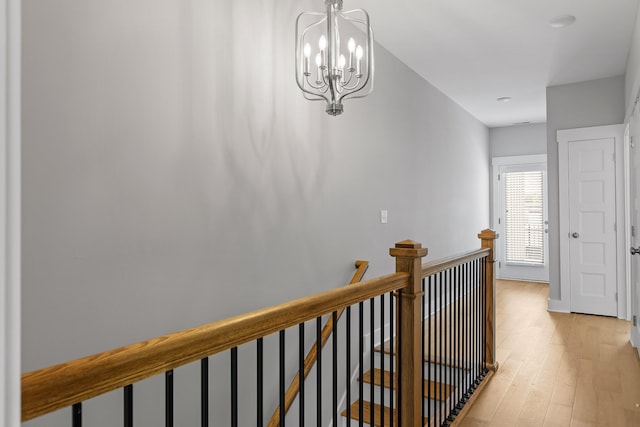 hall with an upstairs landing, light wood-style flooring, and a notable chandelier