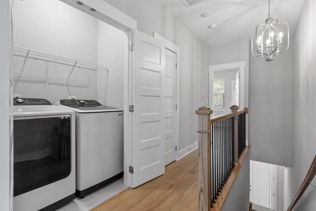 washroom with light wood-type flooring, a chandelier, and washing machine and clothes dryer