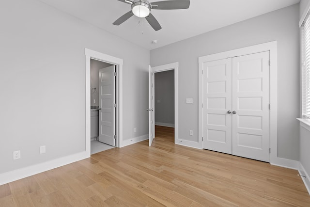 unfurnished bedroom featuring a closet, light wood-style flooring, baseboards, a ceiling fan, and ensuite bath