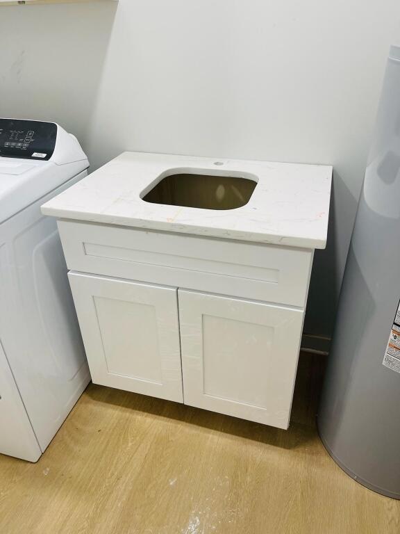 details with light hardwood / wood-style flooring, water heater, washer / dryer, white cabinetry, and light stone counters