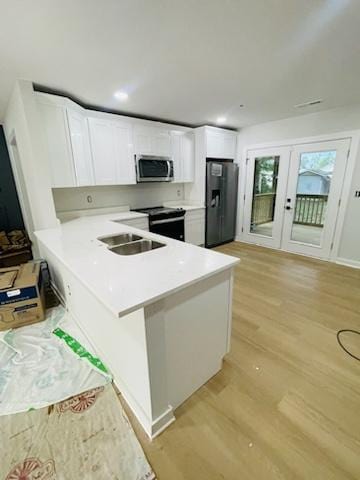 kitchen featuring light wood-type flooring, kitchen peninsula, sink, appliances with stainless steel finishes, and white cabinets