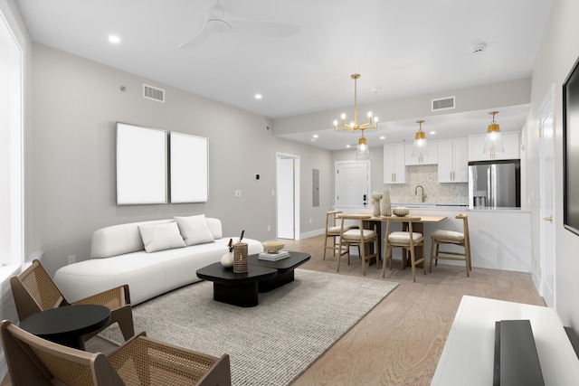 living room featuring light hardwood / wood-style flooring, ceiling fan with notable chandelier, and sink