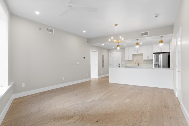 unfurnished living room with ceiling fan with notable chandelier and light hardwood / wood-style flooring