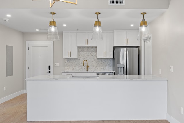 kitchen with backsplash, white cabinets, light hardwood / wood-style flooring, stainless steel fridge, and light stone counters