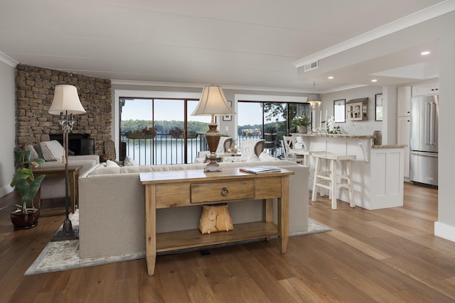 living room featuring crown molding, a stone fireplace, light wood-type flooring, and a water view