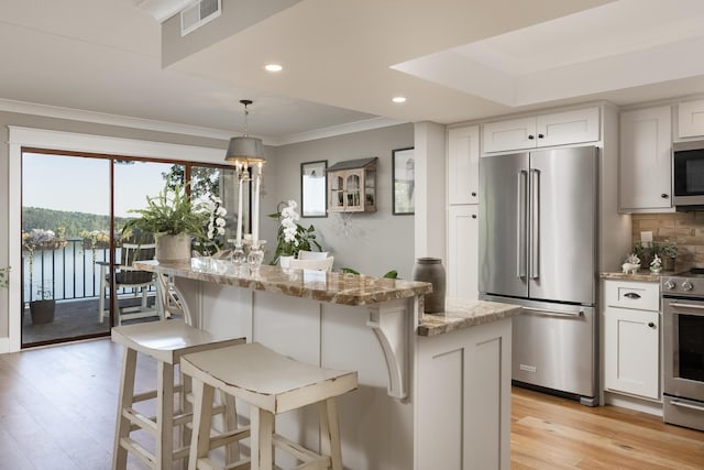 kitchen with white cabinetry, light stone counters, a kitchen island, appliances with stainless steel finishes, and light hardwood / wood-style floors