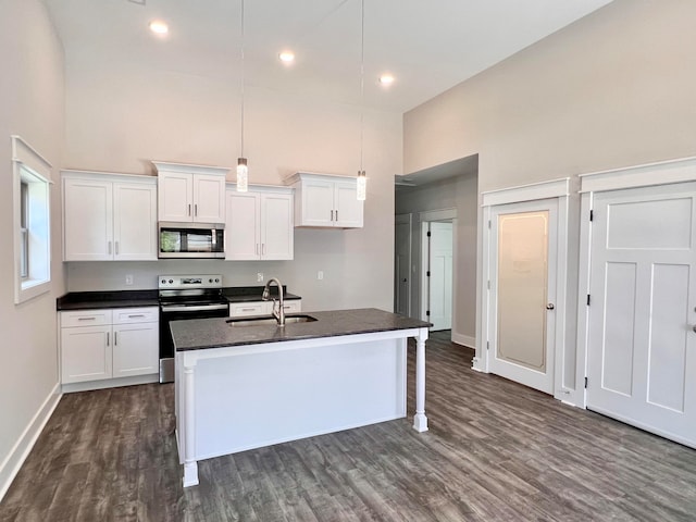 kitchen with dark hardwood / wood-style flooring, a center island with sink, appliances with stainless steel finishes, a towering ceiling, and white cabinets