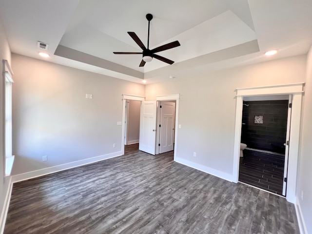 unfurnished bedroom featuring ceiling fan, dark hardwood / wood-style floors, a tray ceiling, and a fireplace